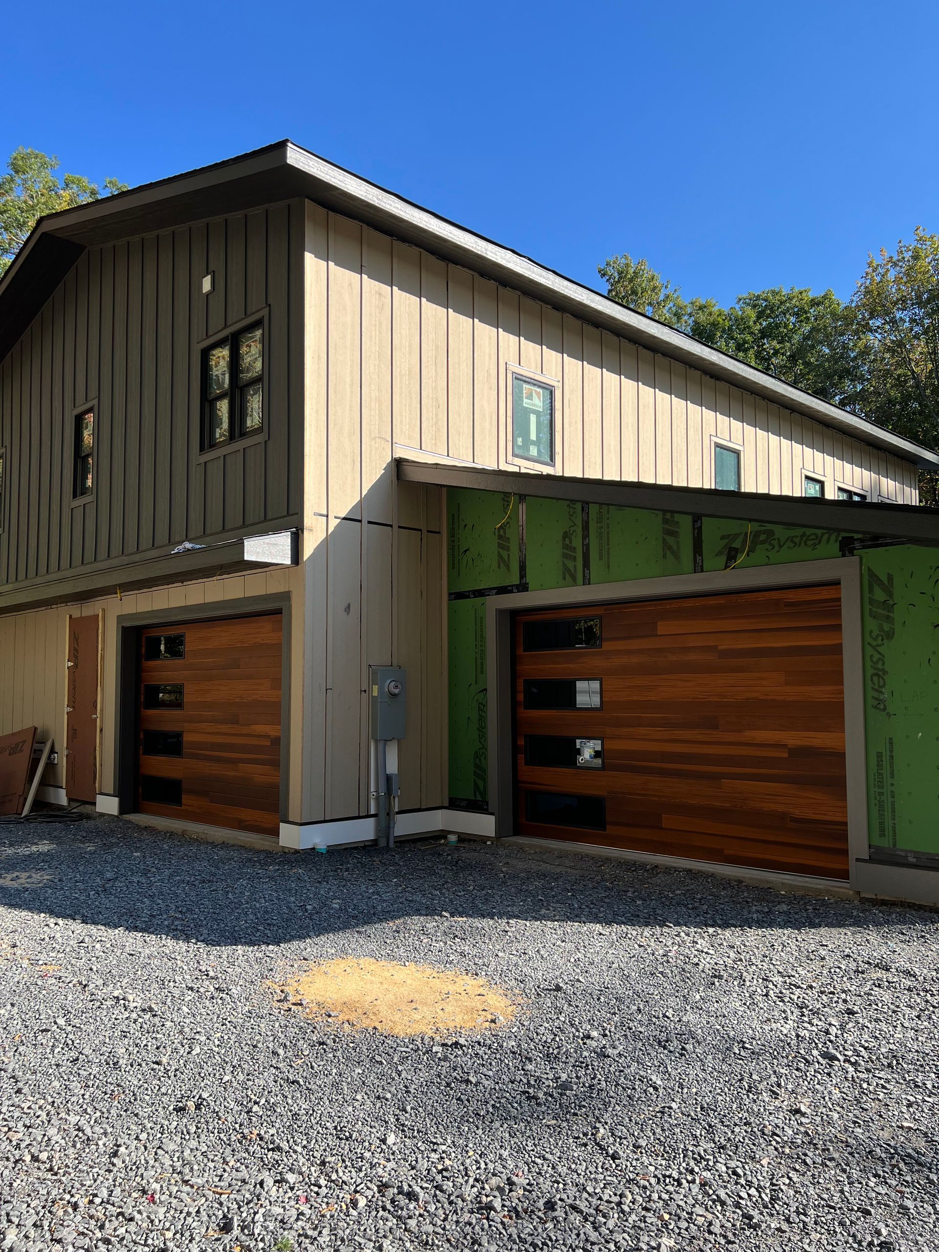 A house under construction with two garage doors and a gravel driveway.
