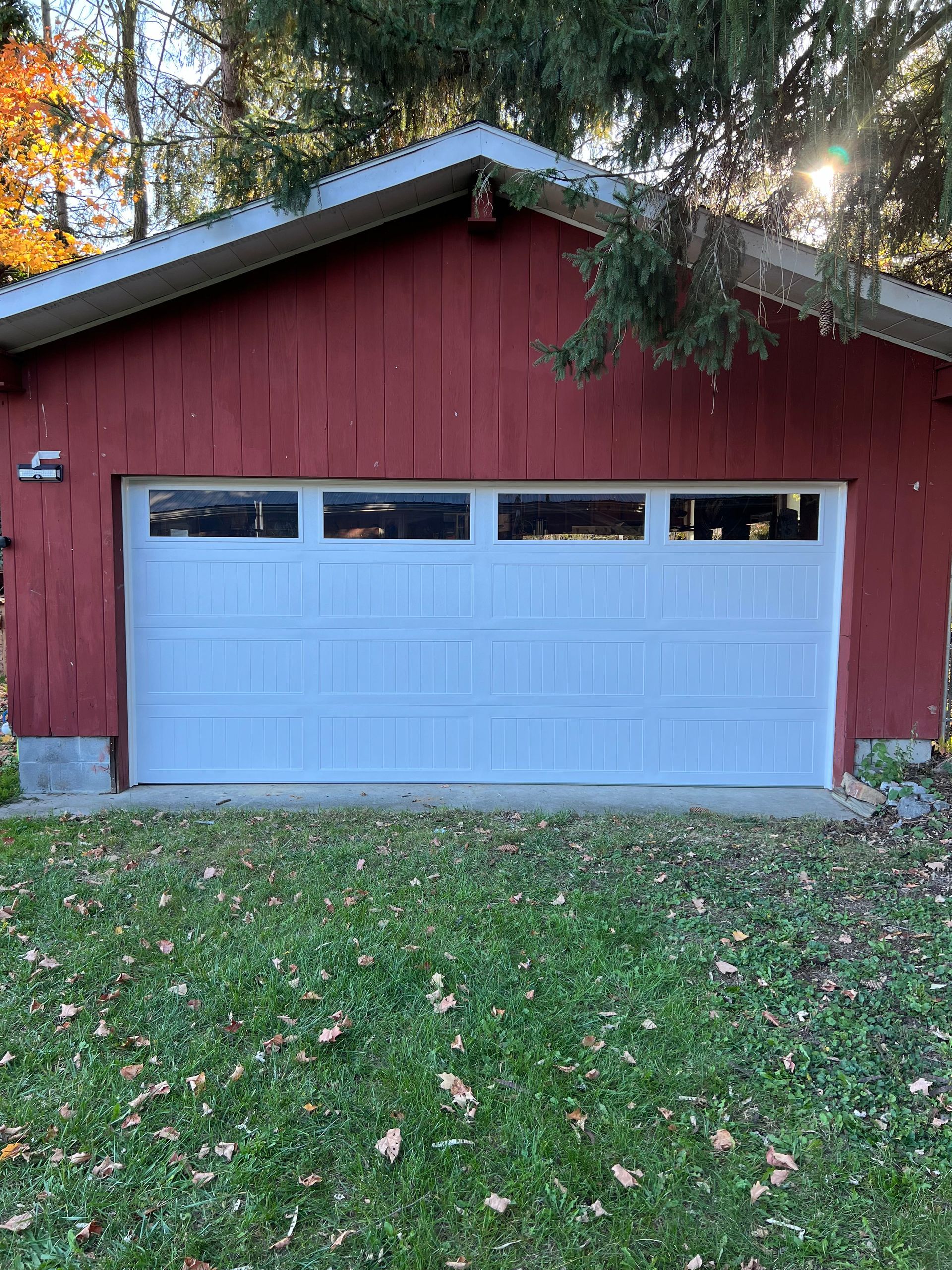 A red garage with a white garage door is sitting on top of a lush green lawn.
