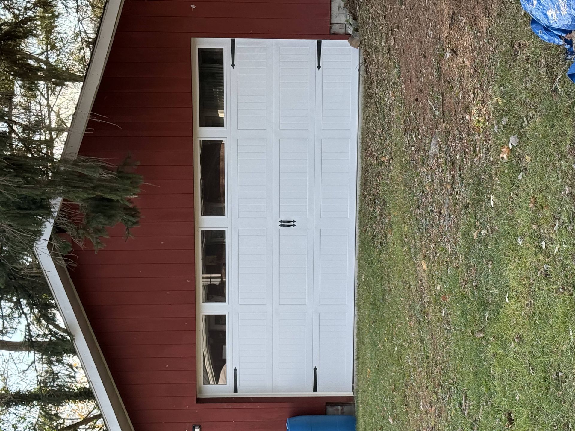 A red garage with white doors and windows is sitting on top of a lush green field.