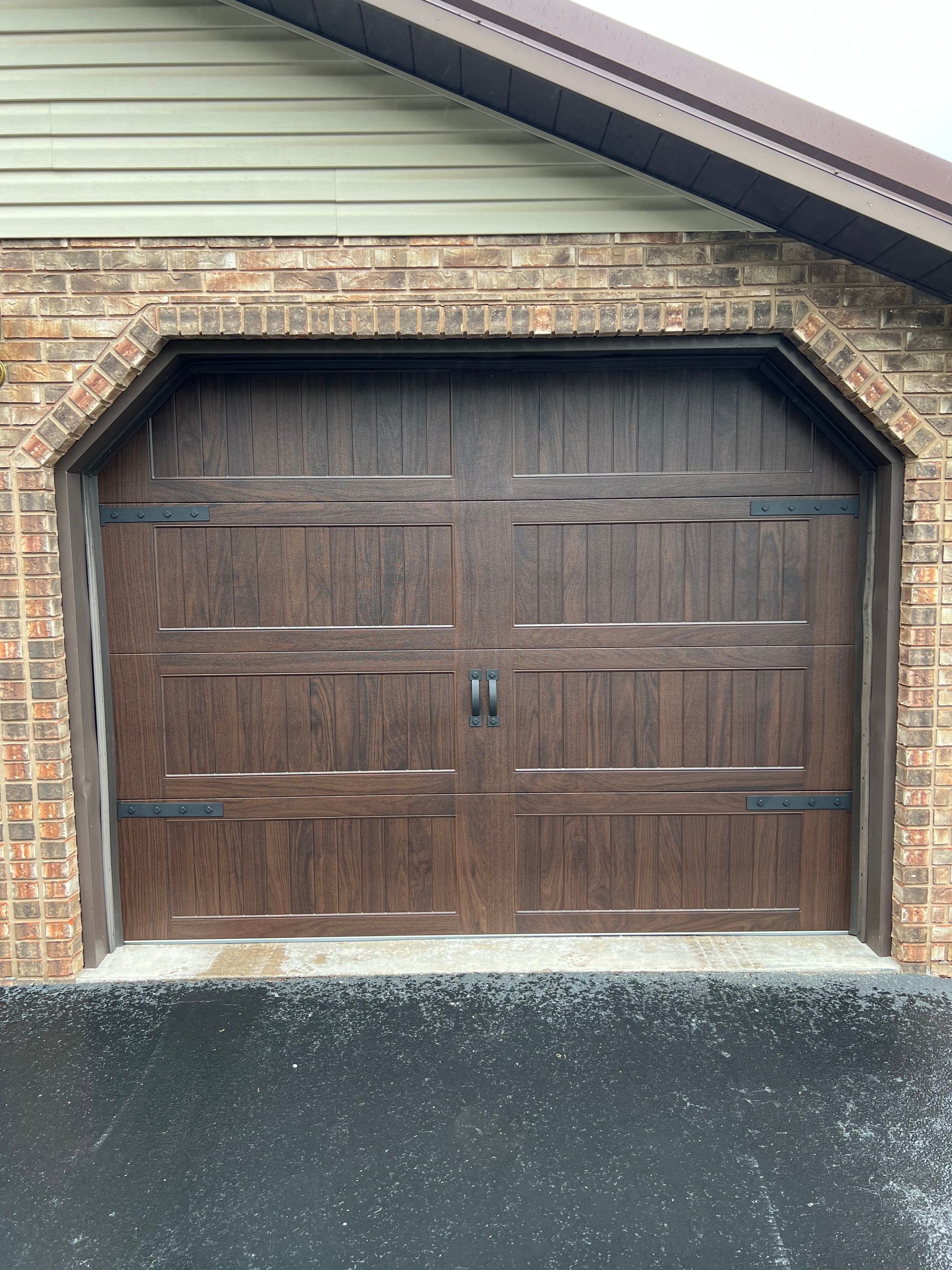 A brown garage door with a brick wall behind it