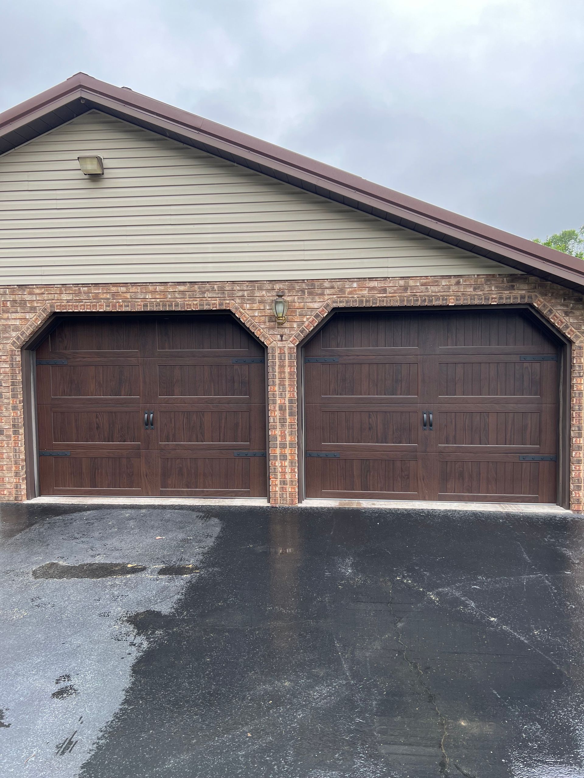 A brick garage with two brown garage doors and a black driveway.