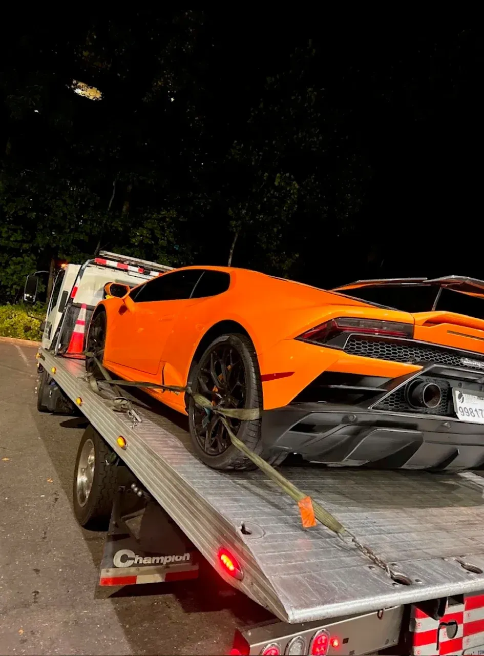 An orange Lamborghini supercar secured by straps onto the flatbed of a tow truck at night.
