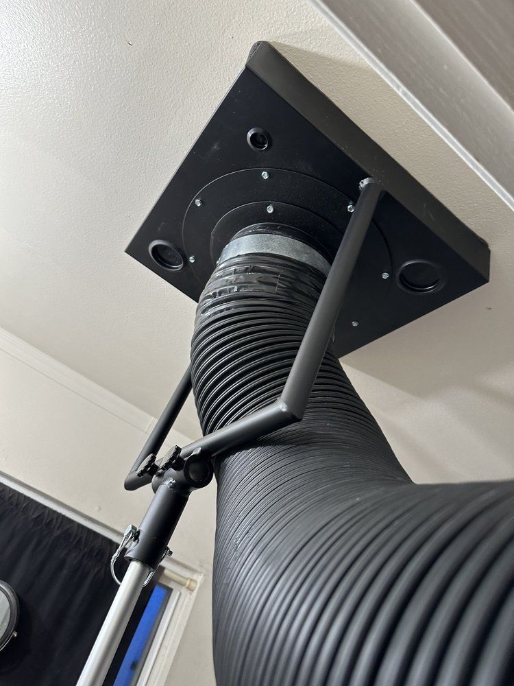 Black ceiling-mounted ventilation duct with flexible hose and strap support, viewed from below