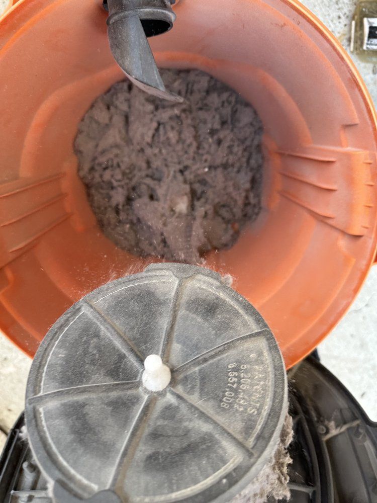 Orange bucket with muddy debris and a gray vent cover inside