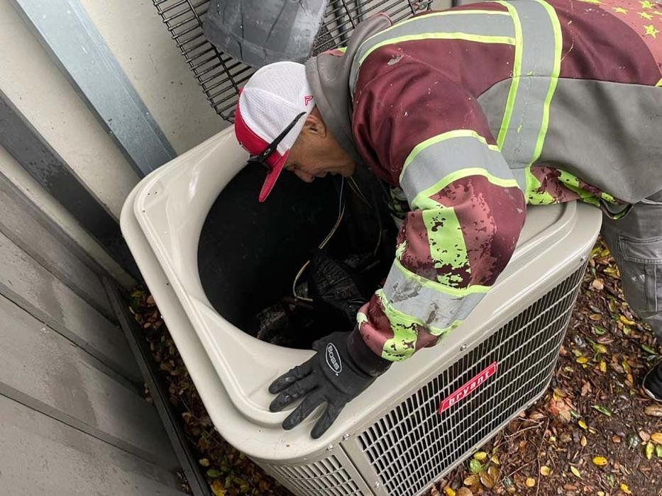 Worker in reflective gear cleaning debris from an outdoor air conditioning unit.