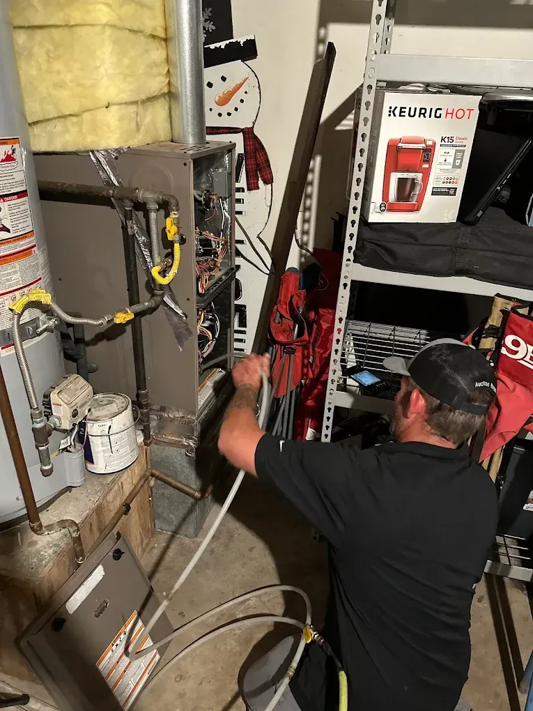 Technician kneeling in a utility room beside pipes and a red KEDRICK tool rack, working near electrical equipment.