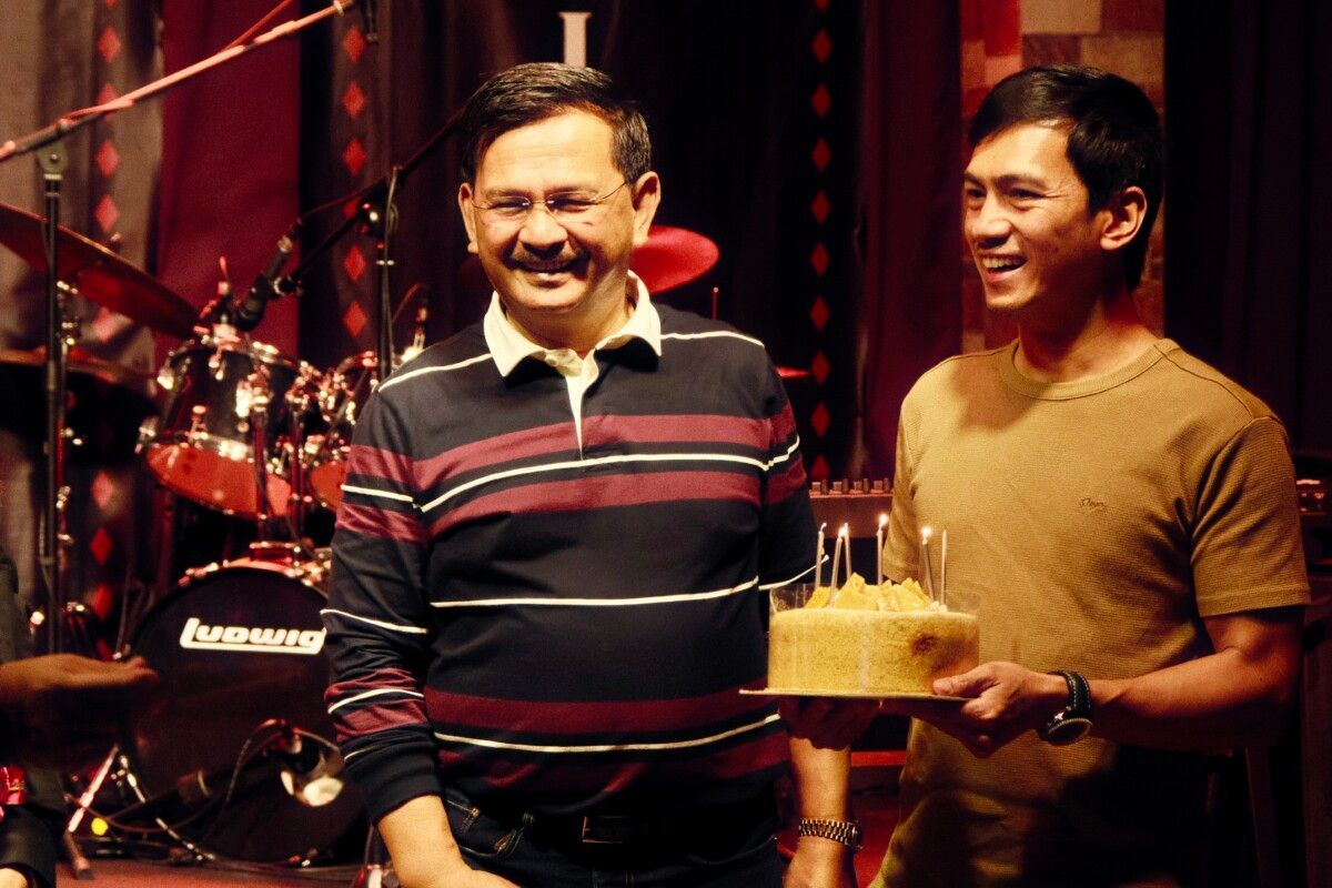 A man is holding a birthday cake in front of a drum set