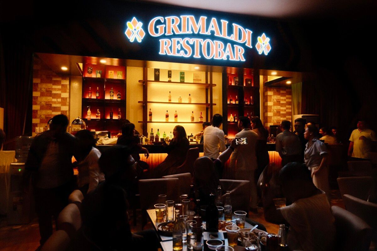A group of people are sitting at tables in front of a sign that says grimaldi restobar