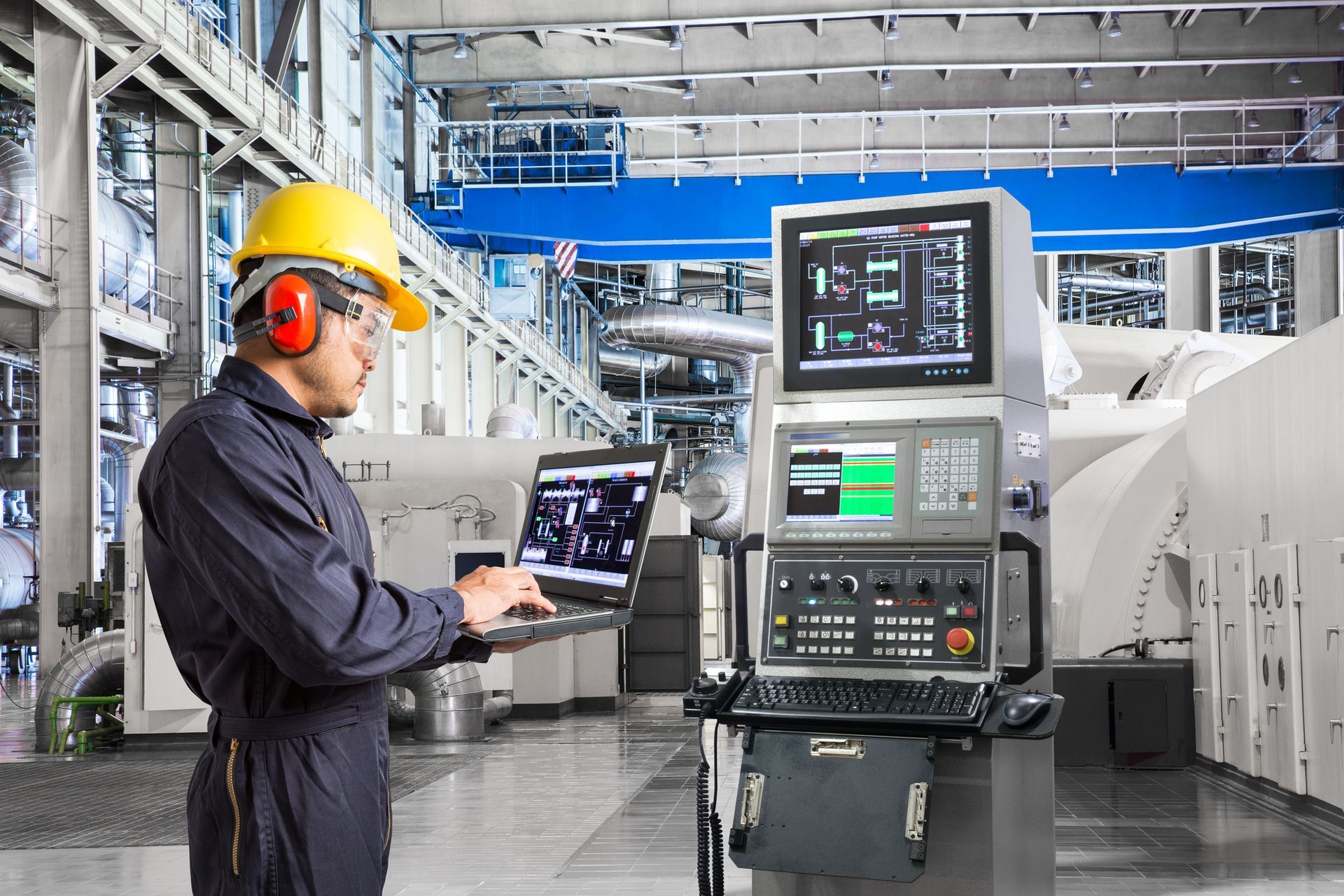 A man in a hard hat is using a laptop in a factory.