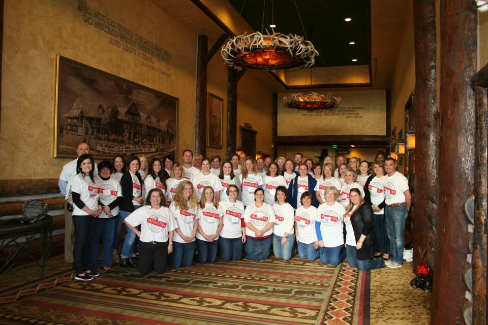 Large group of people wearing matching white shirts, posing in a rustic lobby.