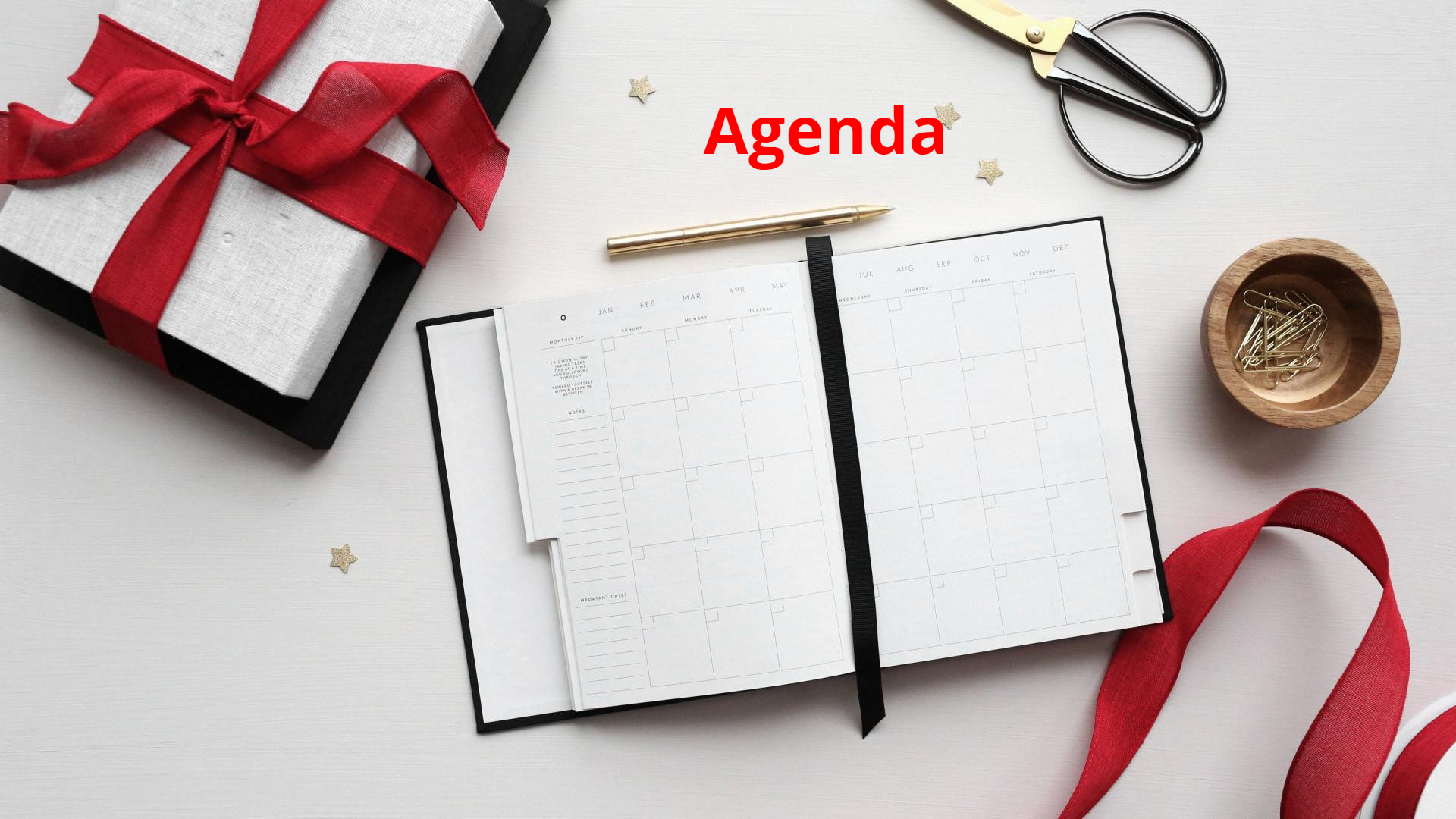 A white gift, open notebook, red ribbon, and gold accents on a white surface with the word