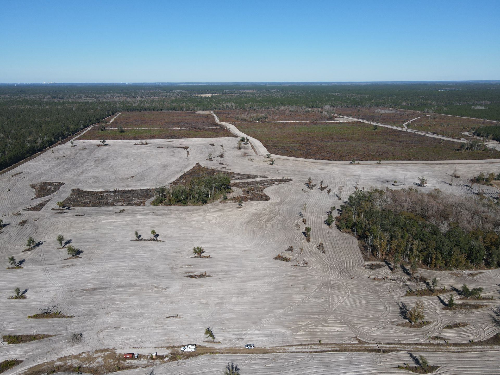 Aerial view of a large, cleared plot of land with patches of brown soil, sparse vegetation, and surrounding forest.