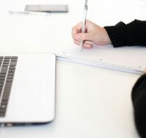 A person is writing in a notebook next to a laptop