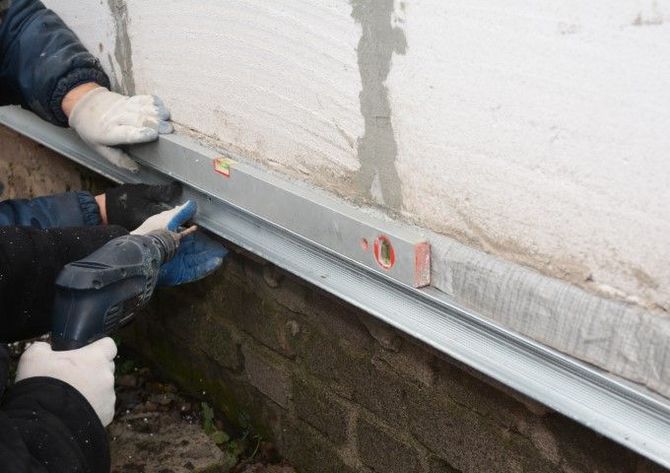 Workers installing a metal flashing strip along a wall with a spirit level.
