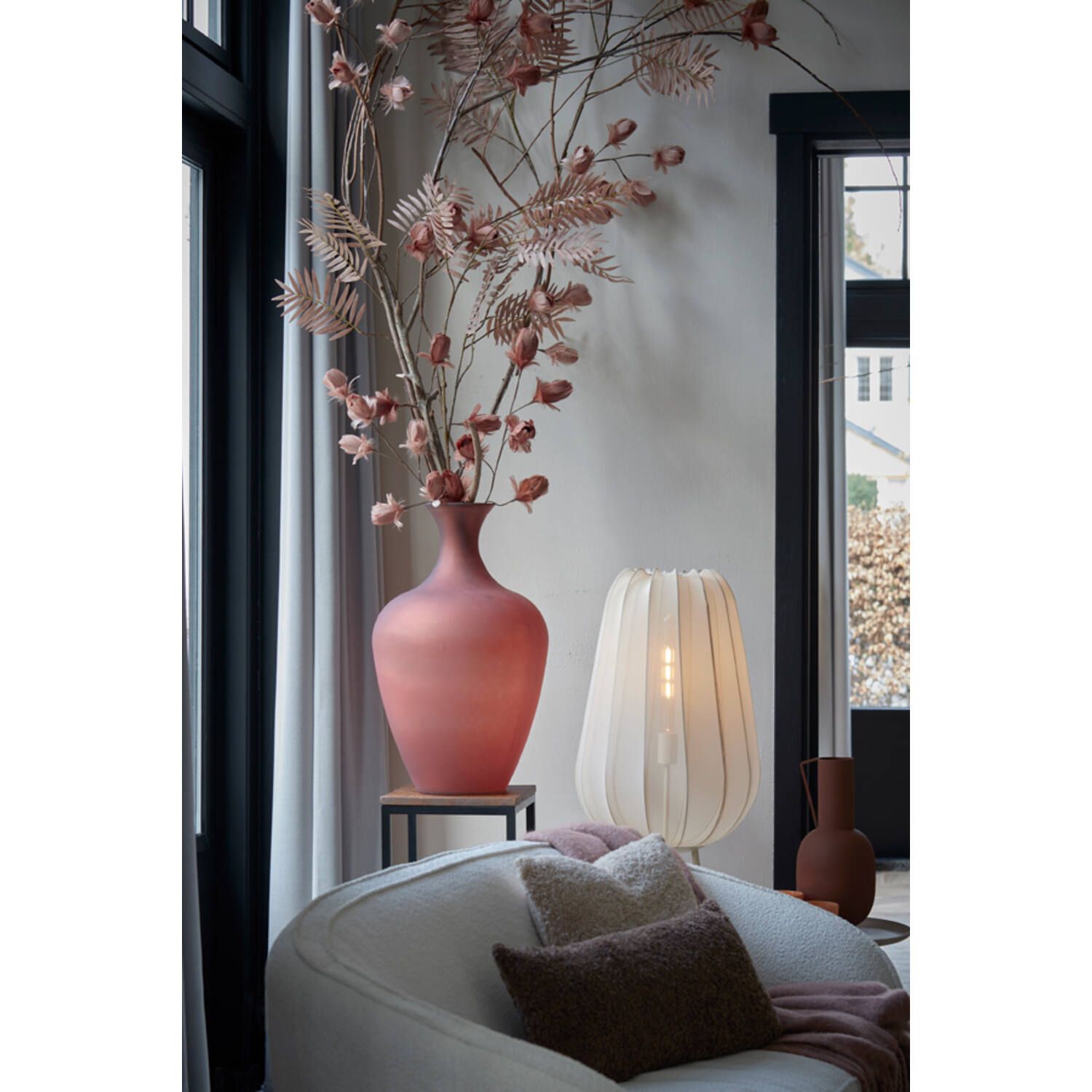 Woonkamerinterieur met een roze vaas, bloemen, een lamp en een fauteuil.