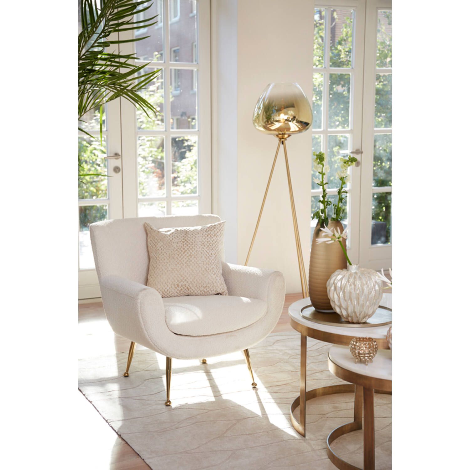 Eetkamerscène: ronde tafel met stoel, gouden accenten, glazen vaas met bloemen en een staande lamp.