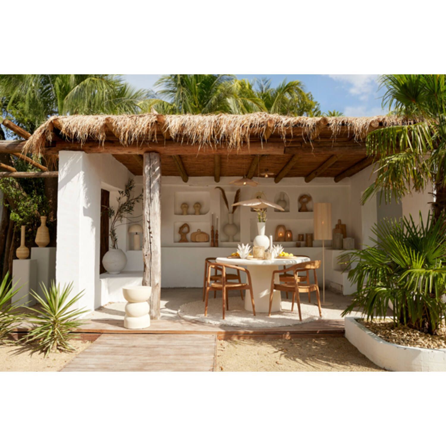 Eetgedeelte buiten met rieten dak, witte muren, houten tafel en stoelen en decoratieve vazen.