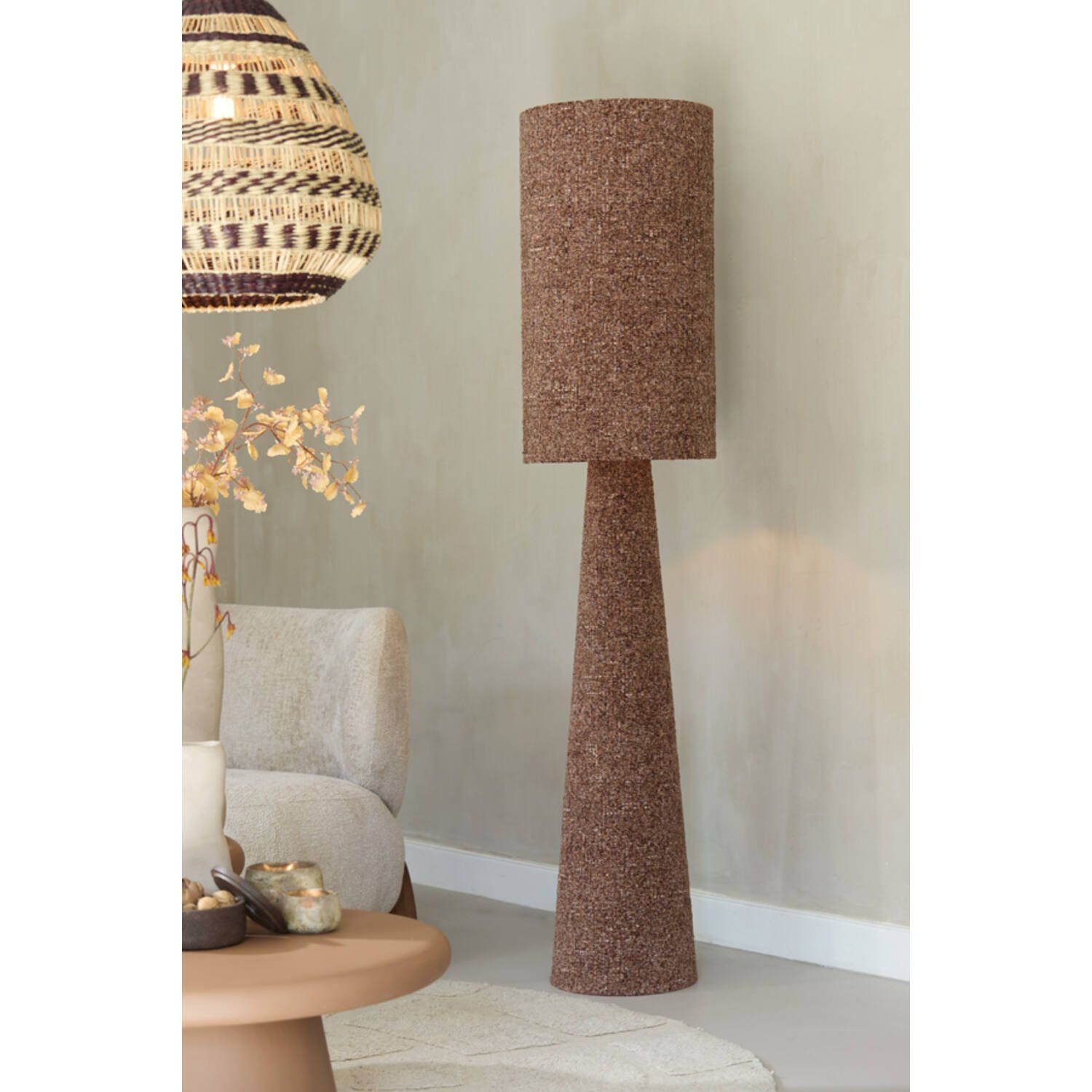 Een staande lamp van kurk tegen een muur, die een kamer in neutrale tinten verlicht.