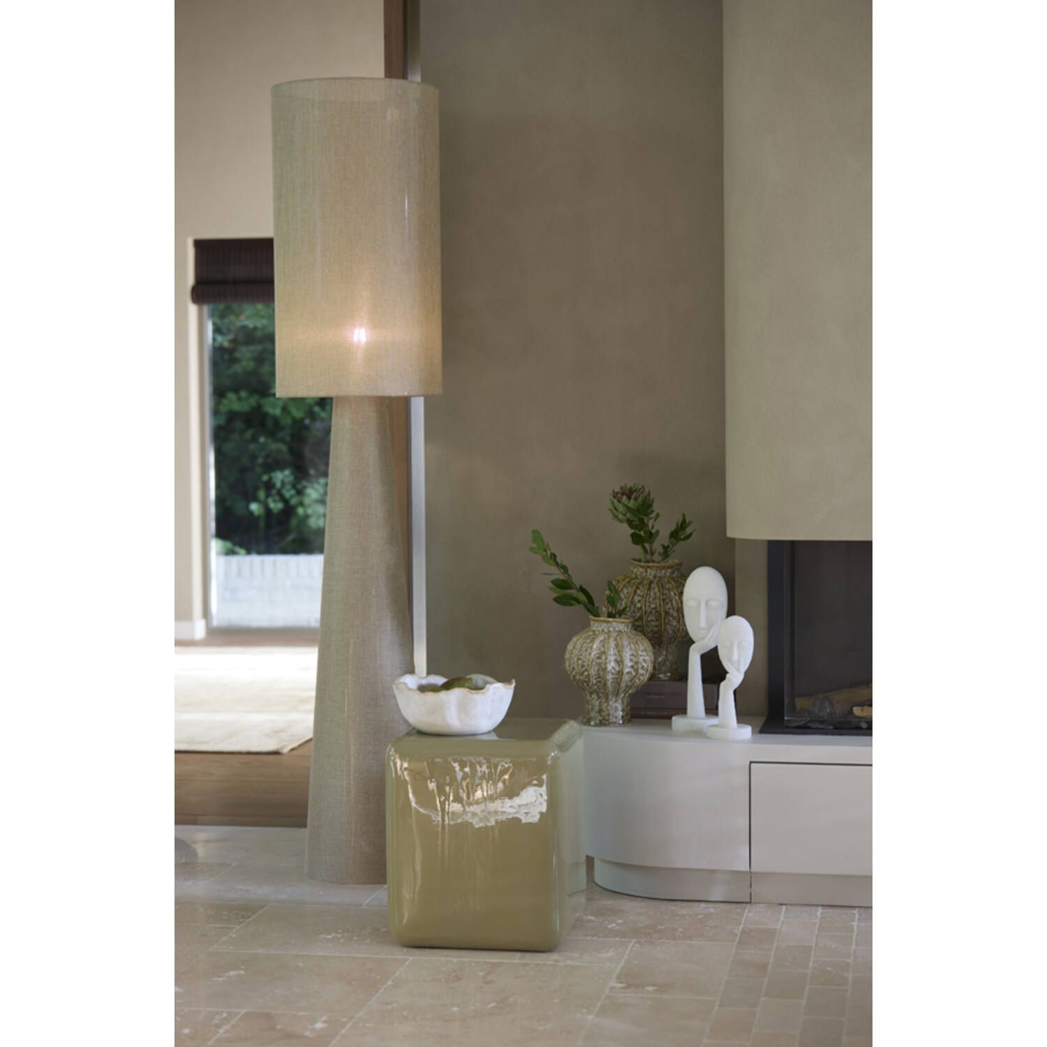 Een hoge staande lamp met een beige kap staat naast een klein tafeltje, een witte vaas en andere decoratieve voorwerpen.