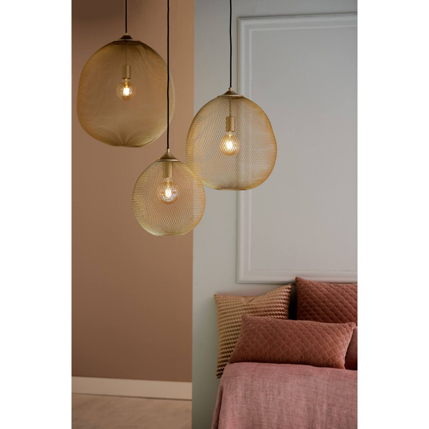 Drie gouden hanglampen met draadframe hangen in een kamer met een bed en sierkussens.