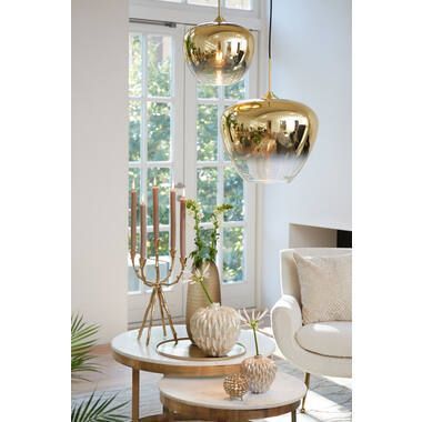 Woonkamer met gouden hanglampen, een salontafel met decoraties en een groot raam.