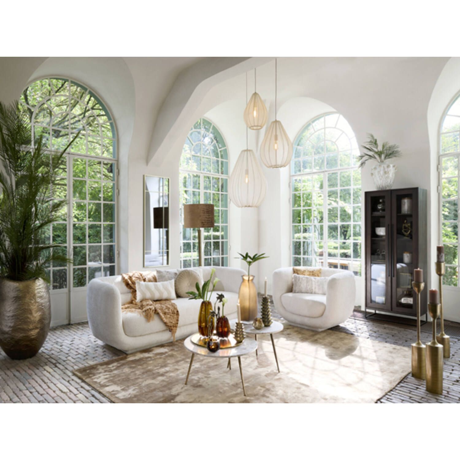 Elegante woonkamer met witte bank, fauteuil, boogvensters en decoratieve objecten.