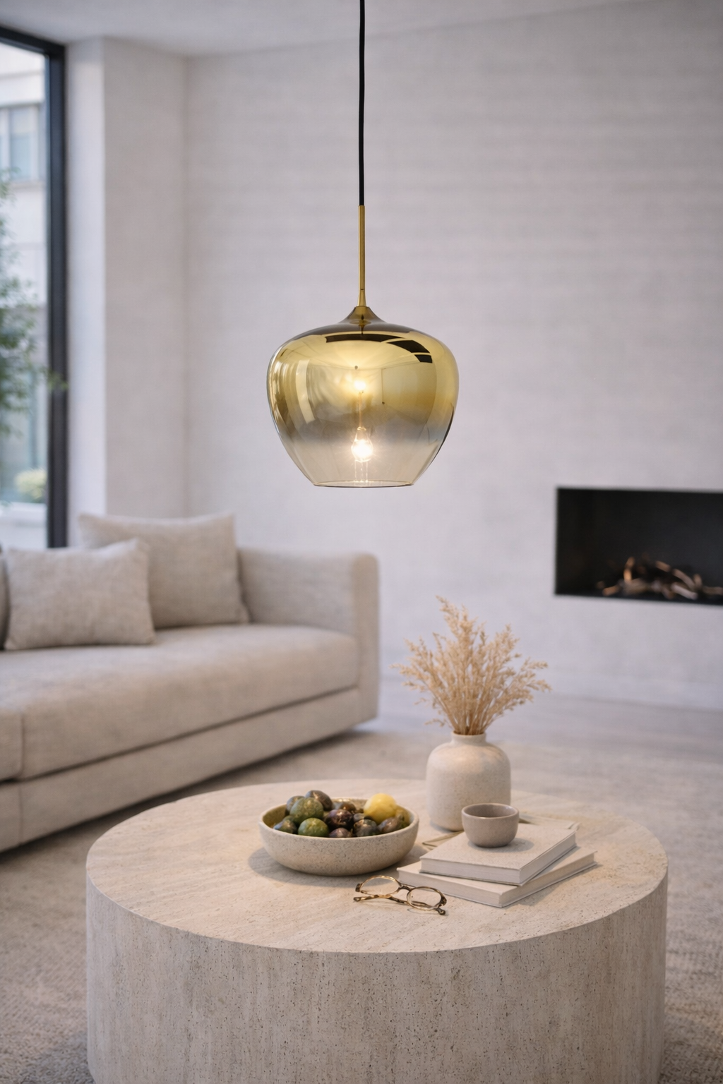 Woonkamer met een hanglamp van goudkleurig en transparant glas, een beige bank en een betonnen salontafel.