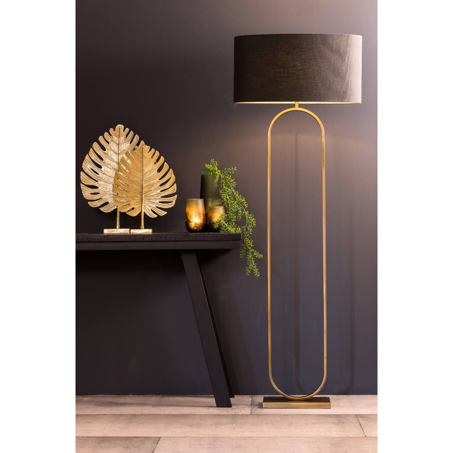 Gouden staande lamp met zwarte kap, naast een zwarte tafel met bladgouddecoratie en kaarsen.