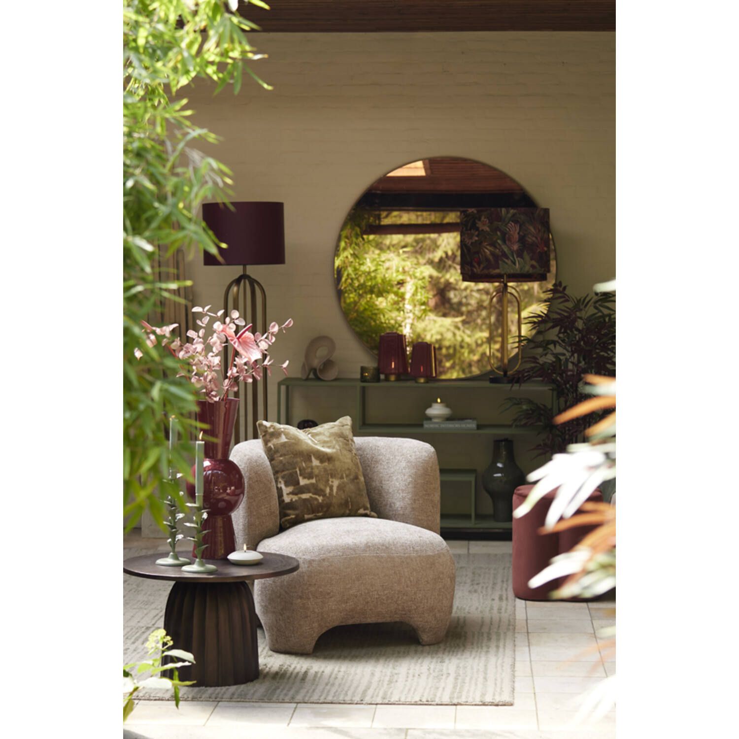 Gezellige buitenruimte met fauteuil, bijzettafel, spiegel en planten in neutrale tinten.