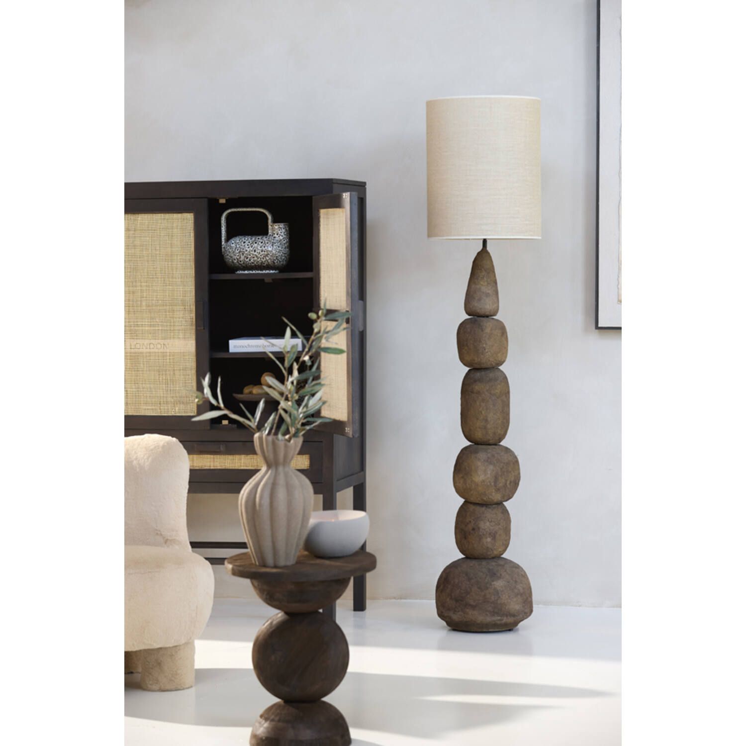 Houten vloerlamp met een ontwerp van gestapelde stenen, naast een donkere kast met een geweven front.