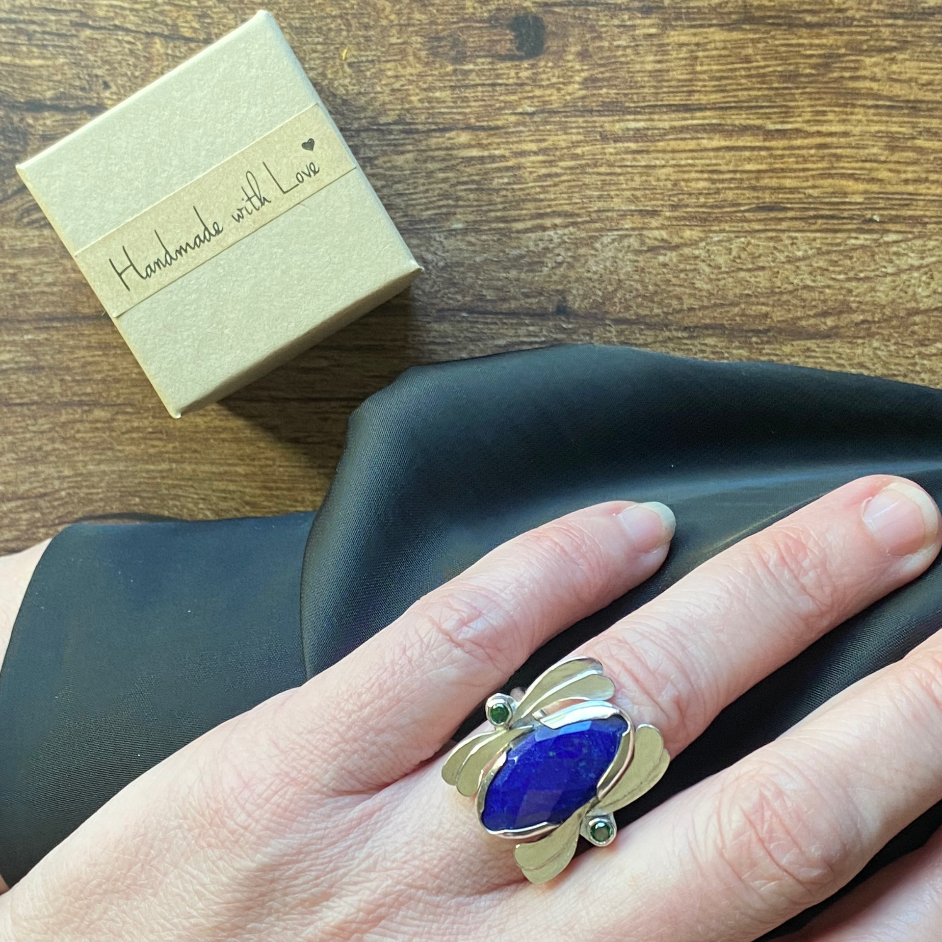 Hand holding a silver butterfly ring with a blue gemstone, next to a gift box. Wild Sunflower Silver Handmade Jewelry