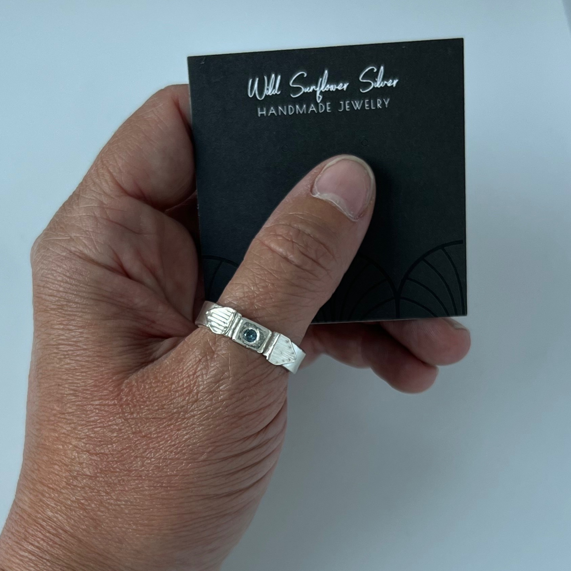 Person's hand holding a black jewelry card with a silver ring on the thumb.