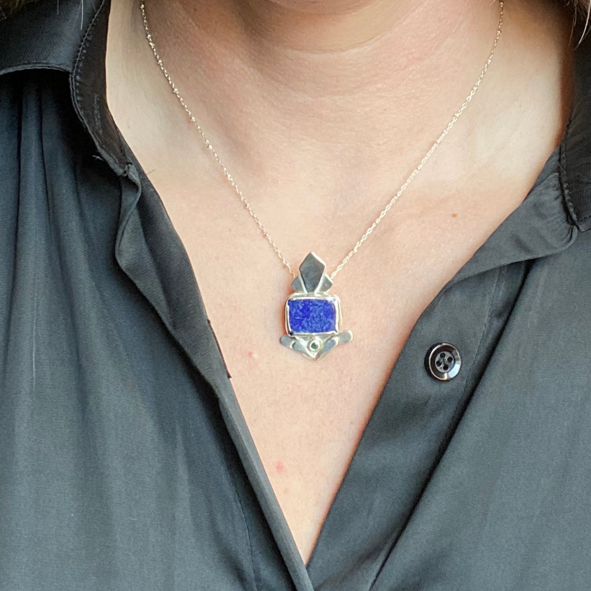 Silver pendant necklace with a blue stone, held in a person's hand. Wild Sunflower Silver Handmade Jewelry