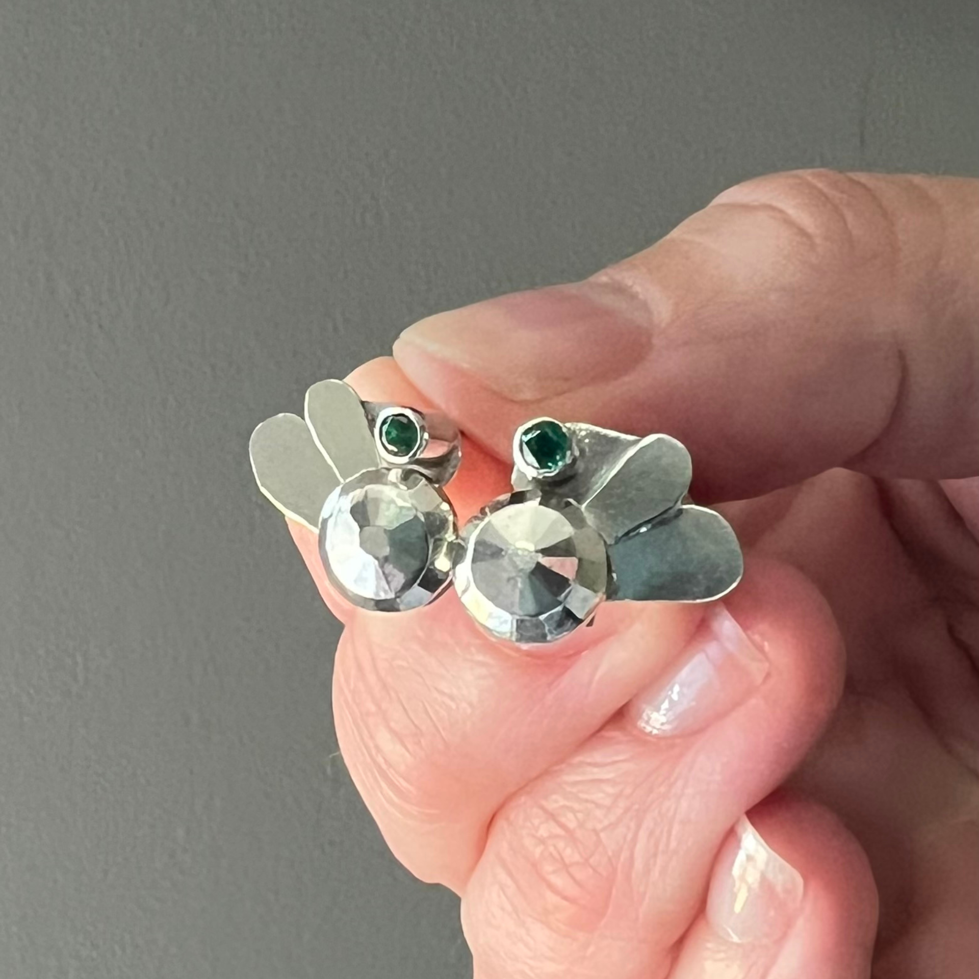 Close-up of a person's ear with a gold bee-shaped earring, featuring a green gem. Wild Sunflower Silver Handmade Jewelry