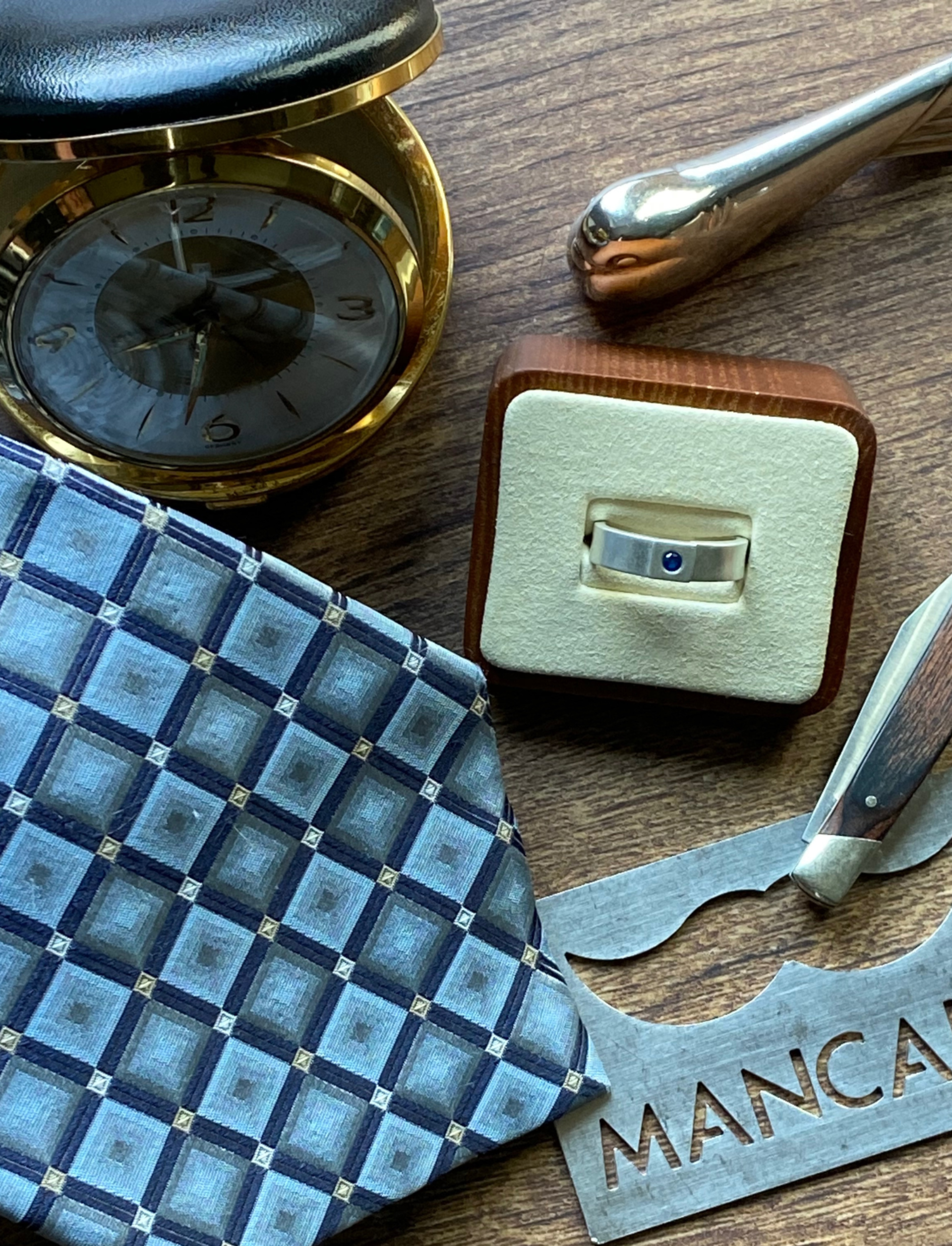 A collection of men's accessories: watch, ring, tie, cufflinks, and knife on a wooden surface.
