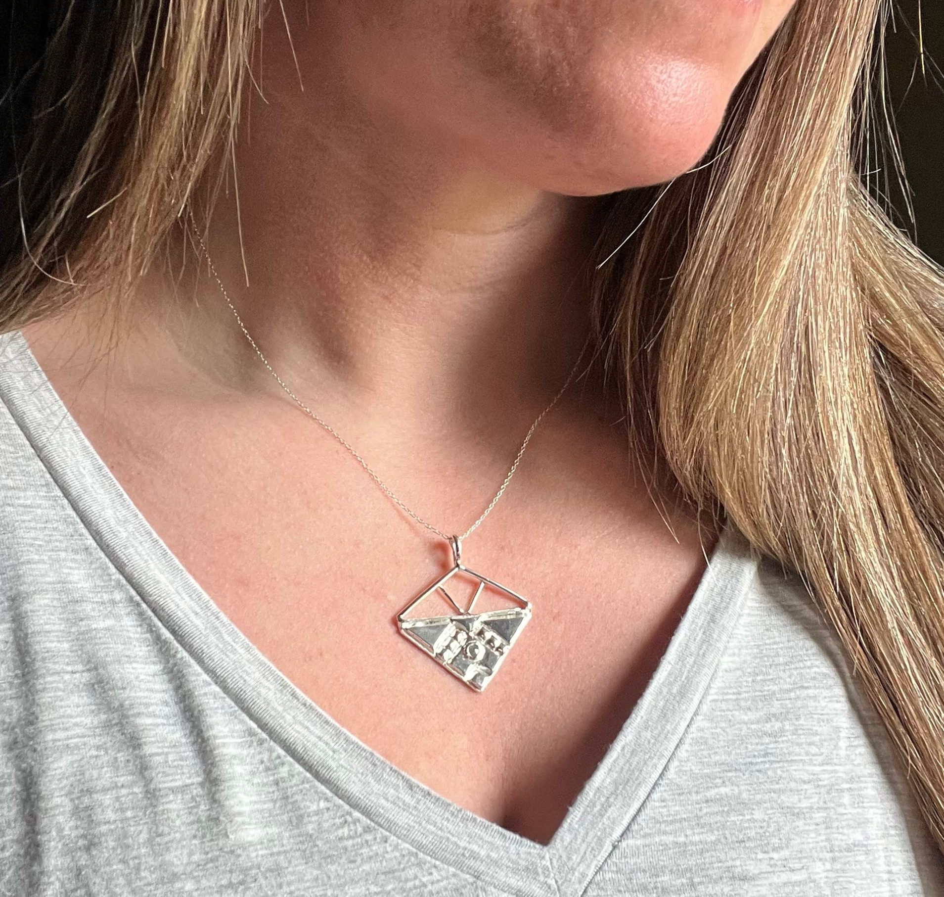 Woman wearing a silver pendant necklace with a geometric, open design. Wild Sunflower Silver Handmade Jewelry
