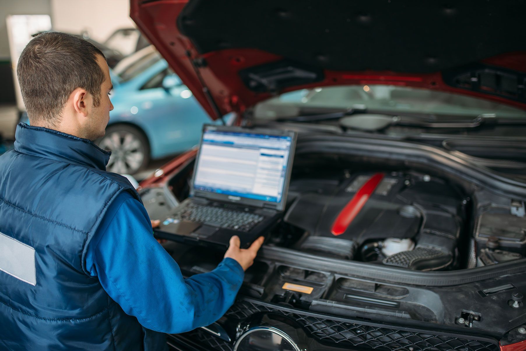 A man is using a laptop computer under the hood of a car.