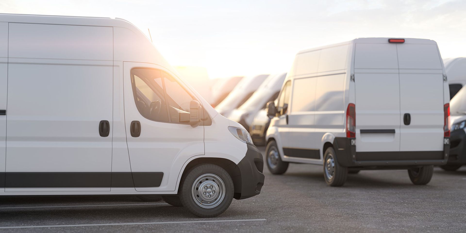 A row of white vans parked next to each other in a parking lot.