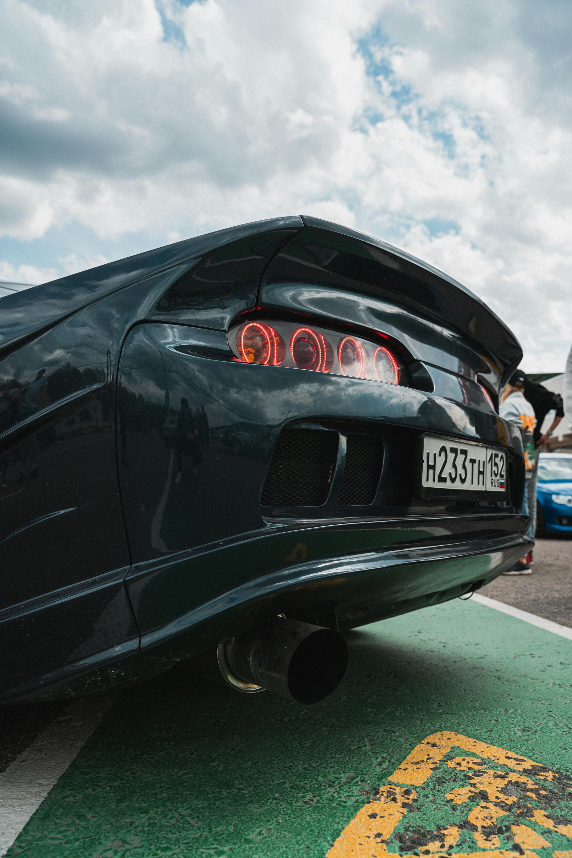 The rear end of a black sports car is parked on a green curb.
