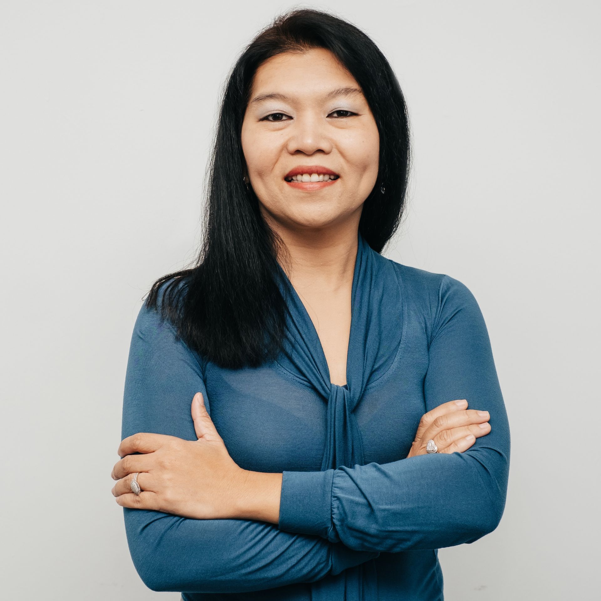 A woman in a blue shirt is smiling with her arms crossed