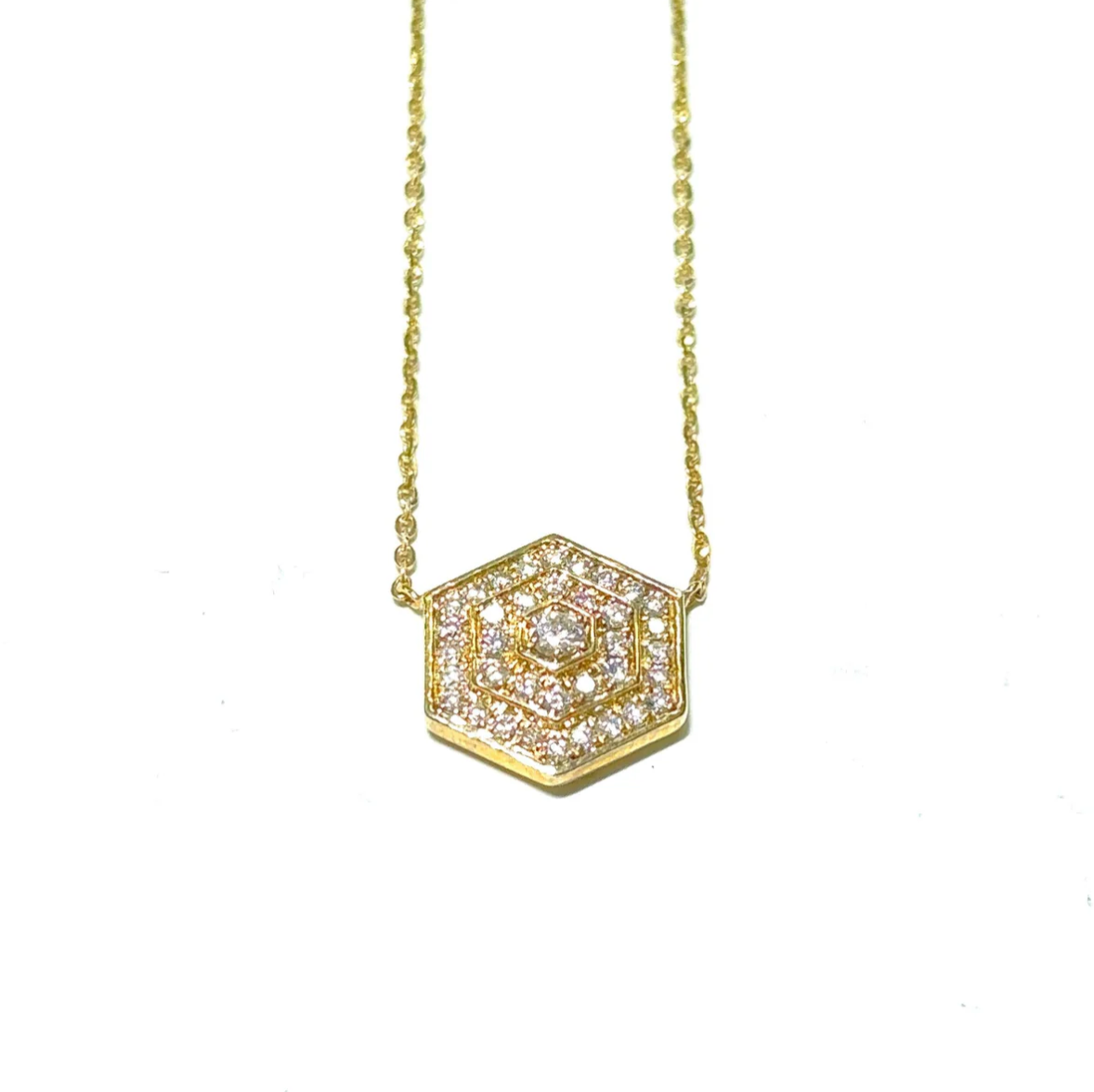A gold necklace with a hexagon shaped pendant on a chain