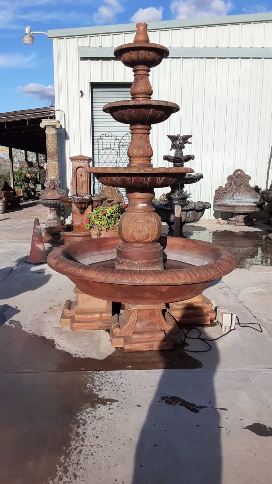 Rusty tiered stone fountain in an outdoor yard beside a white building, with a large basin and decorative carvings