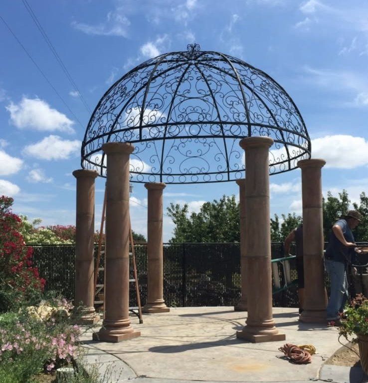 Decorative wrought-iron gazebo on stone patio with columns under a blue sky