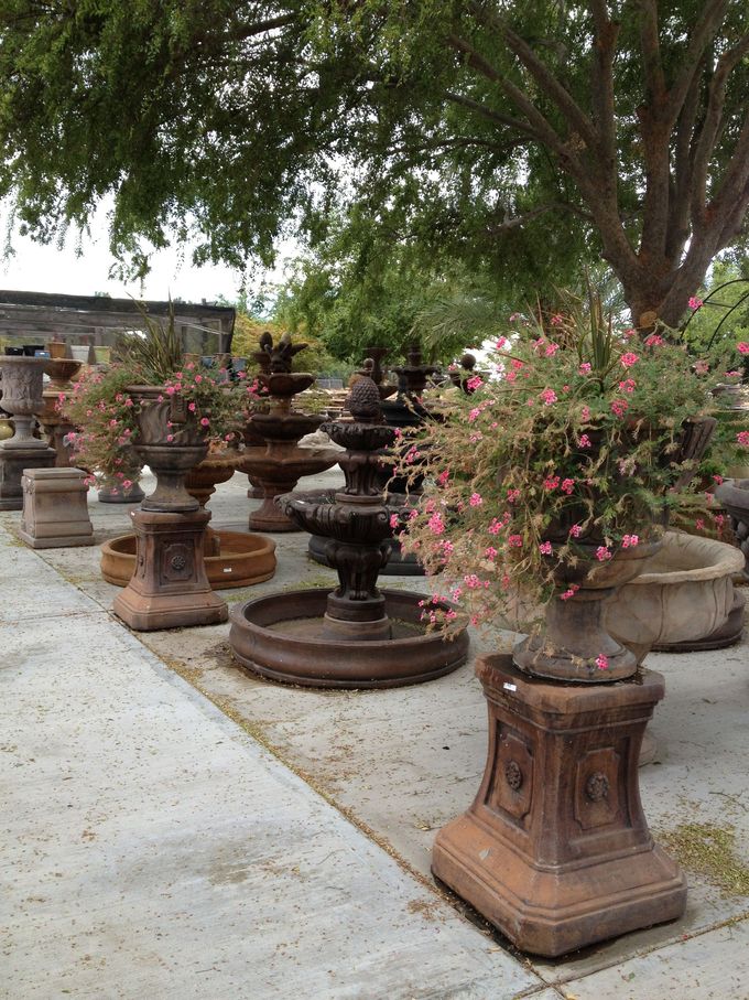 Row of decorative stone fountains and planters along a garden walkway under trees
