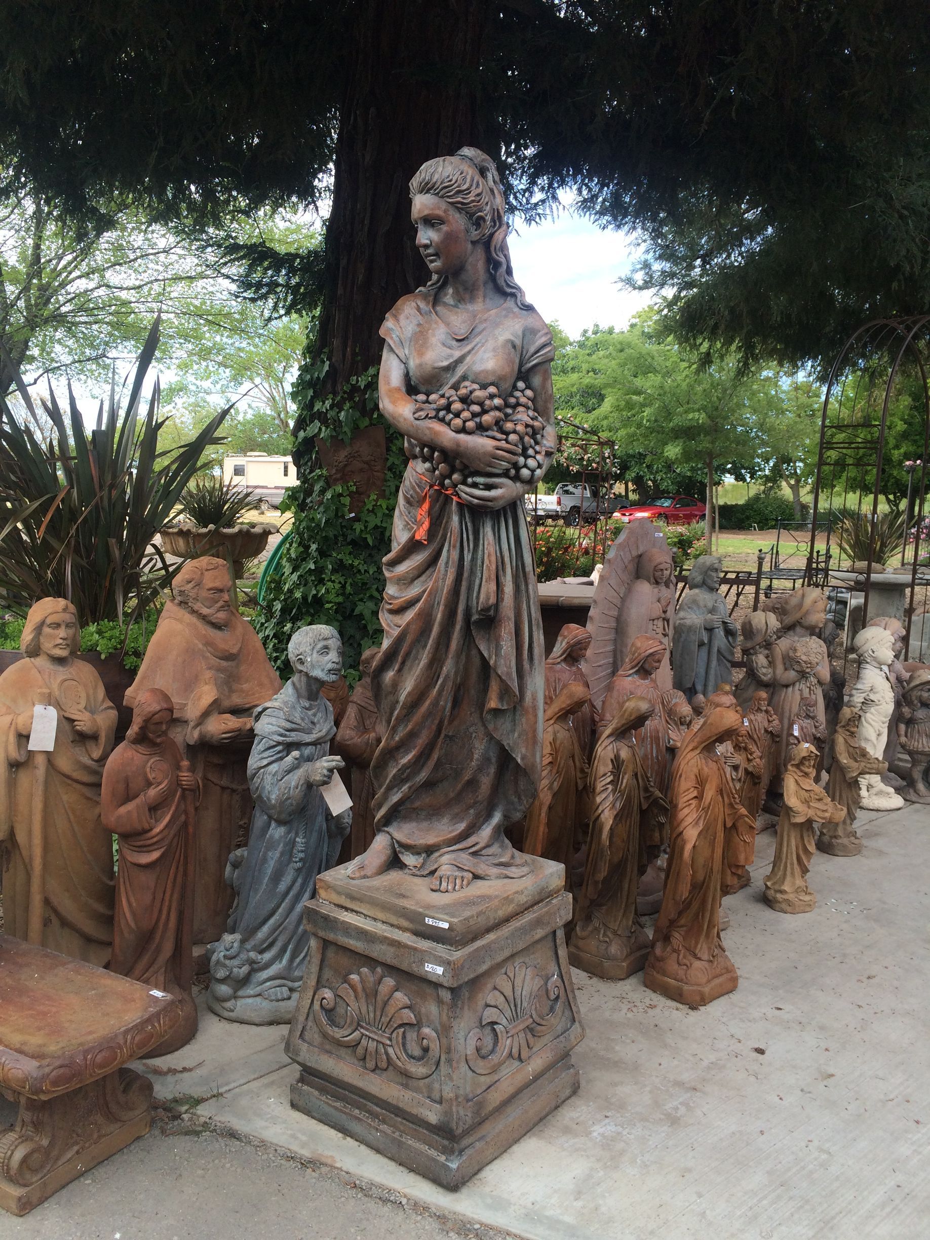 Outdoor display of weathered human sculptures on pedestals beneath trees