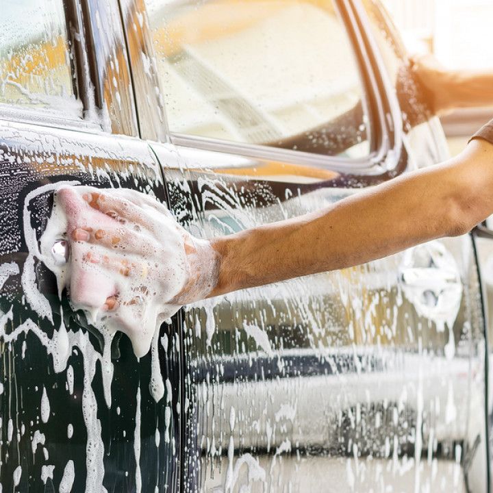 Person washing a black car door with a soapy sponge.