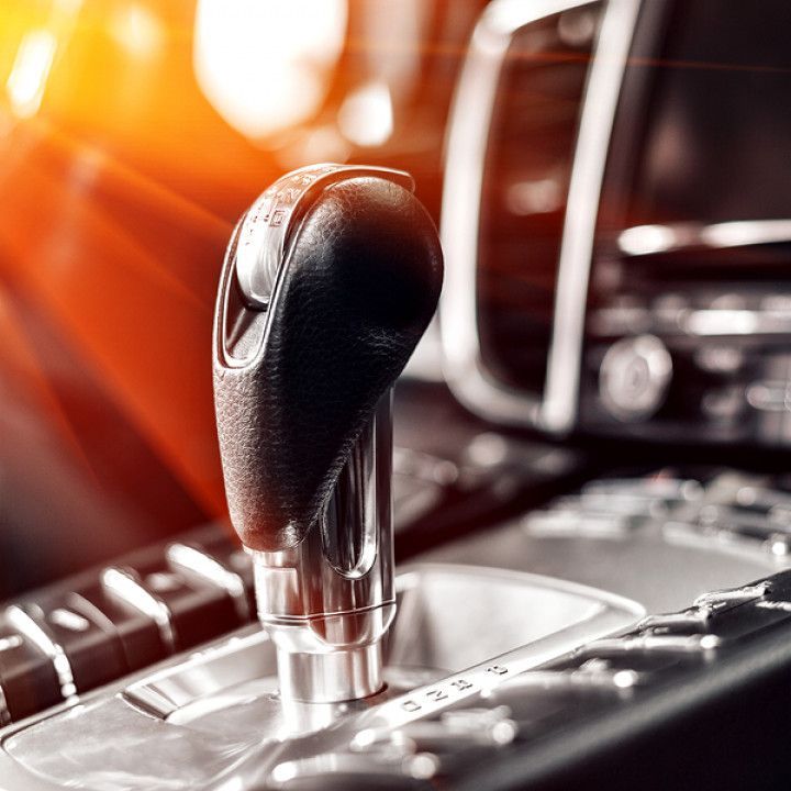 Close-up of a car's automatic gear shift lever, black leather and chrome, with sunlight streaming in.