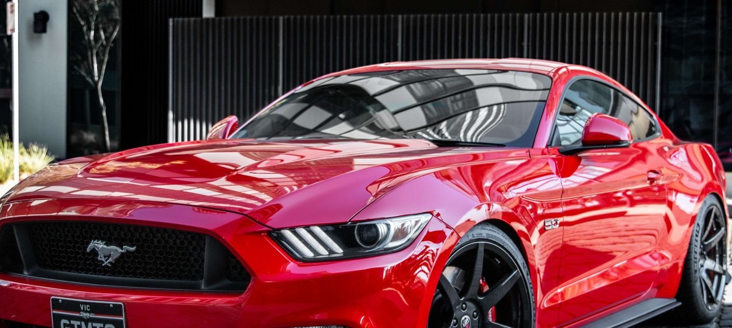 Red Ford Mustang car parked in front of a modern building with black rims.