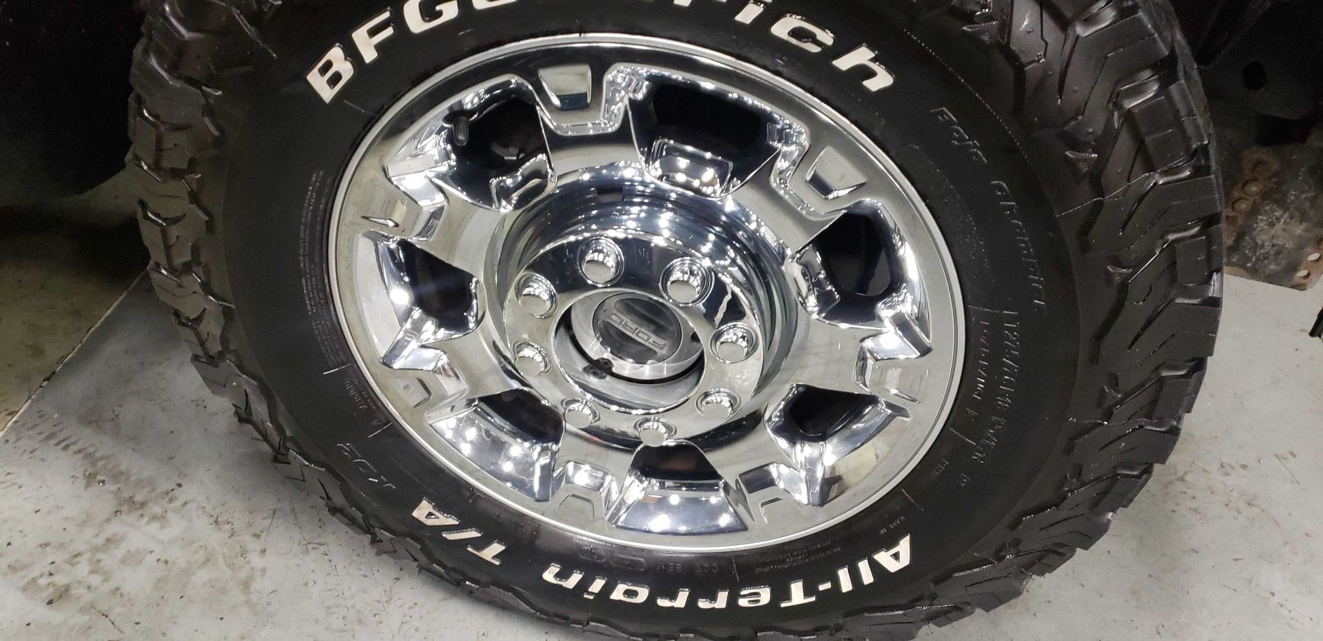 Shiny chrome truck wheel with black tire and white lettering.