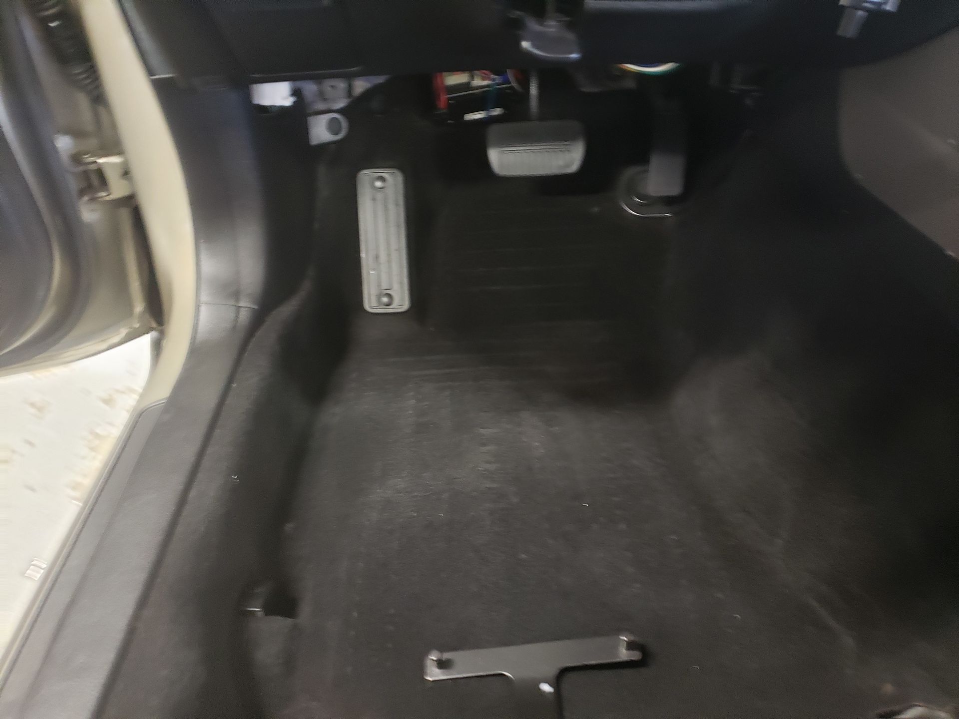 Interior of a car; accelerator and brake pedals visible. Black floor mat and a metal foot rest.